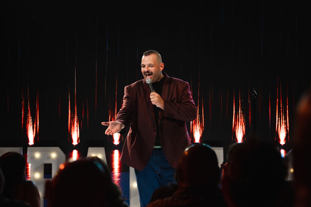 Daniel Franzese in a maroon jacket working the crowd, sparks falling on the LED wall behind him