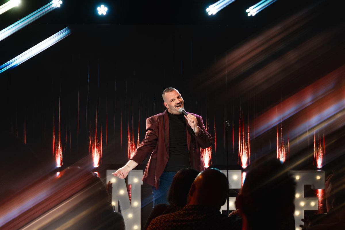 Daniel Franzese smiling on stage under streaking stage lights during the taping