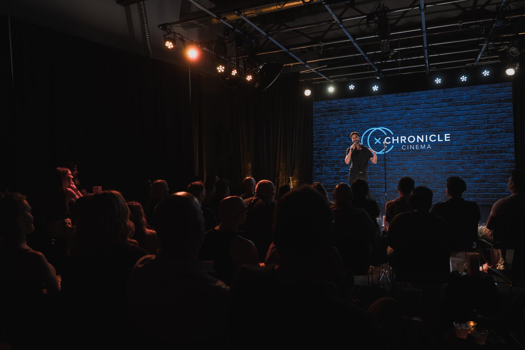 Producer Marc Singer on the Studio C stage with a microphone, speaking to a sold out crowd in front of the LED wall showing the Chronicle Cinema mark on blue brick