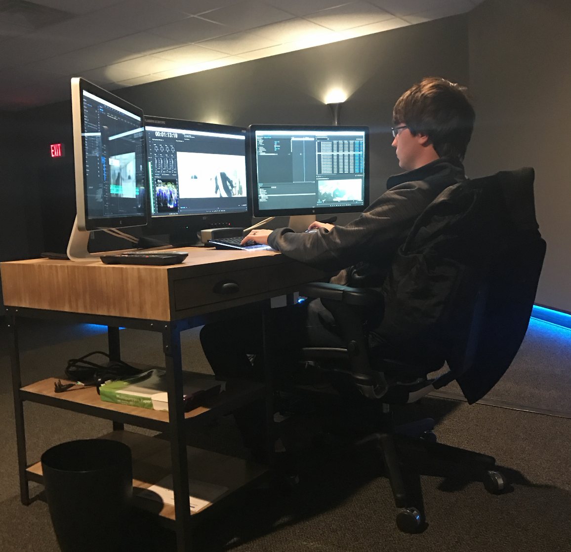 Ken Lutz at a three monitor edit desk in Chronicle&rsquo;s downtown office, cutting a project in a dim room with blue accent lighting