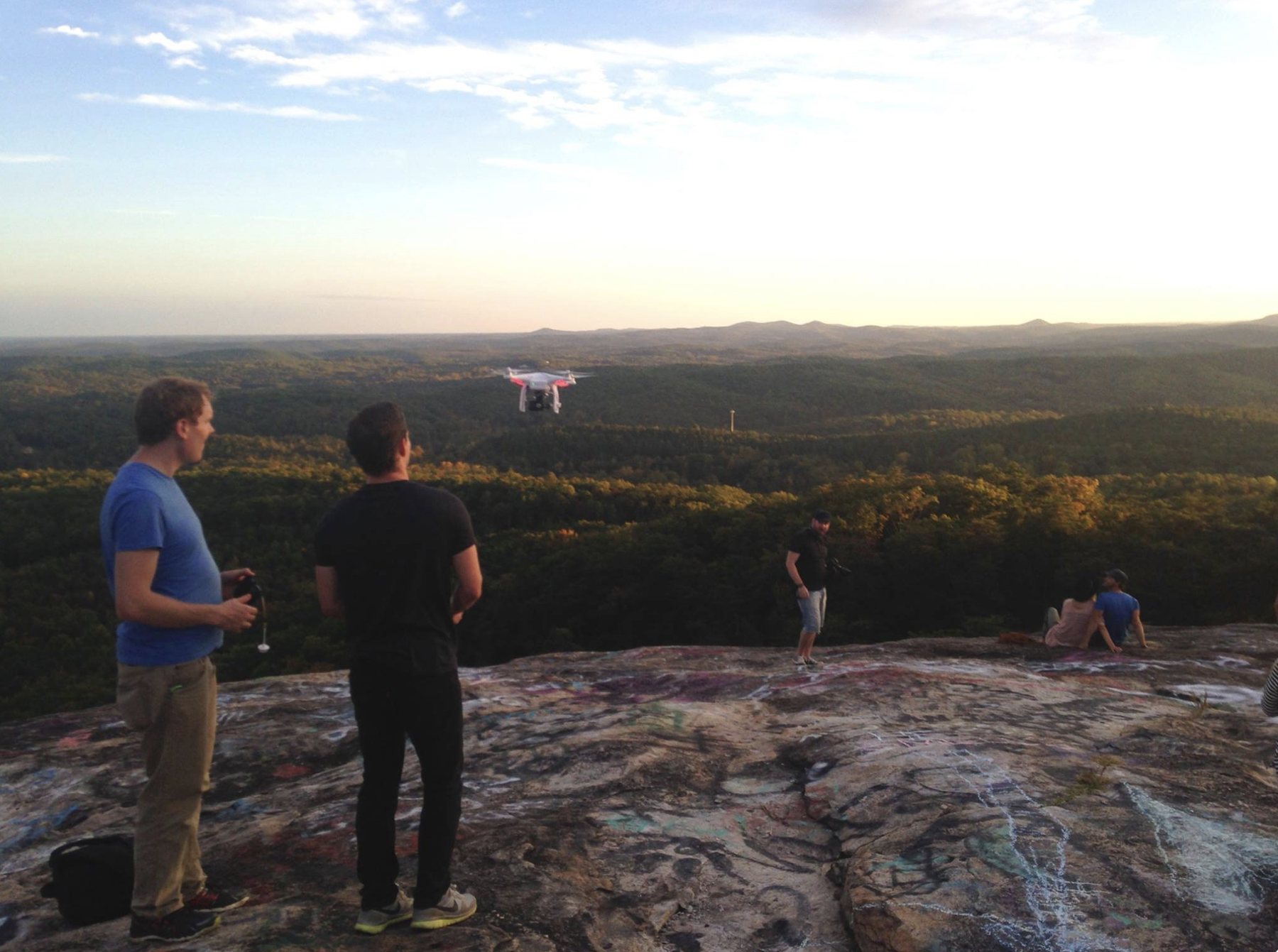 Zach and Sam standing on a rock outcrop flying a drone over forested hills outside Greenville, South Carolina