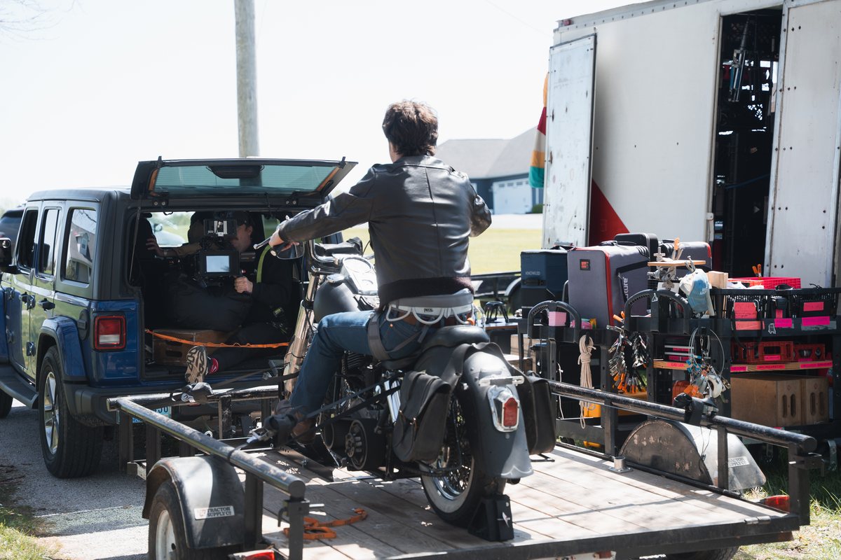 A rider on a motorcycle mounted to a process trailer at night, filmed by a harnessed camera operator.