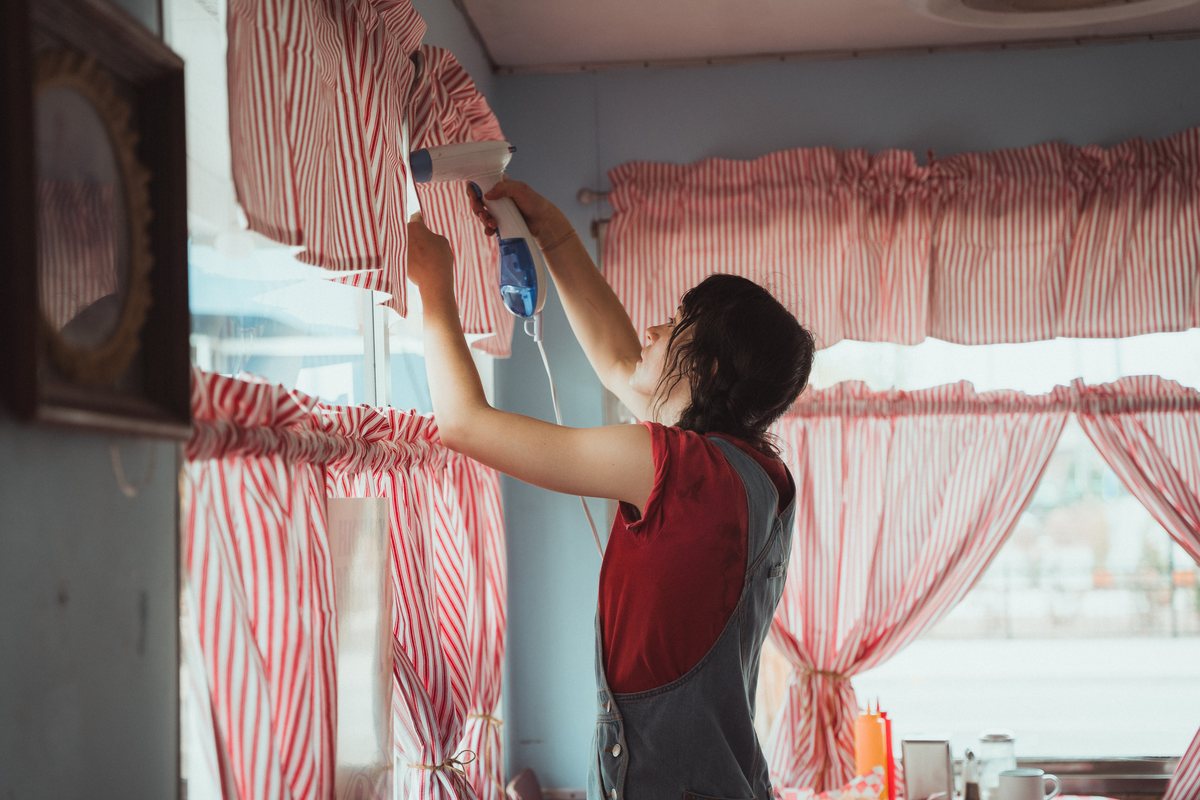 Production designer Sally Wegert hangs curtains inside the diner set.