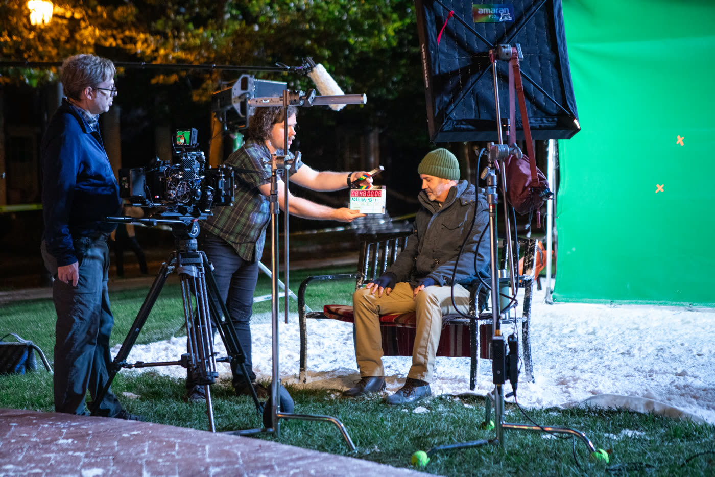 A camera technician holds a digital slate in front of the Arri Alexa camera with fake snow and a green screen.